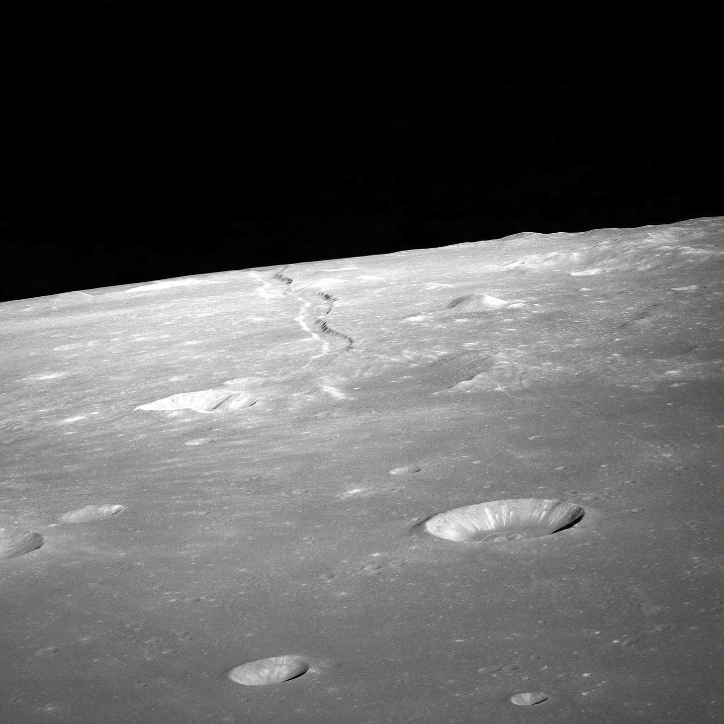A photo of the lunar surface, showing several craters of various sizes, against a black starless sky