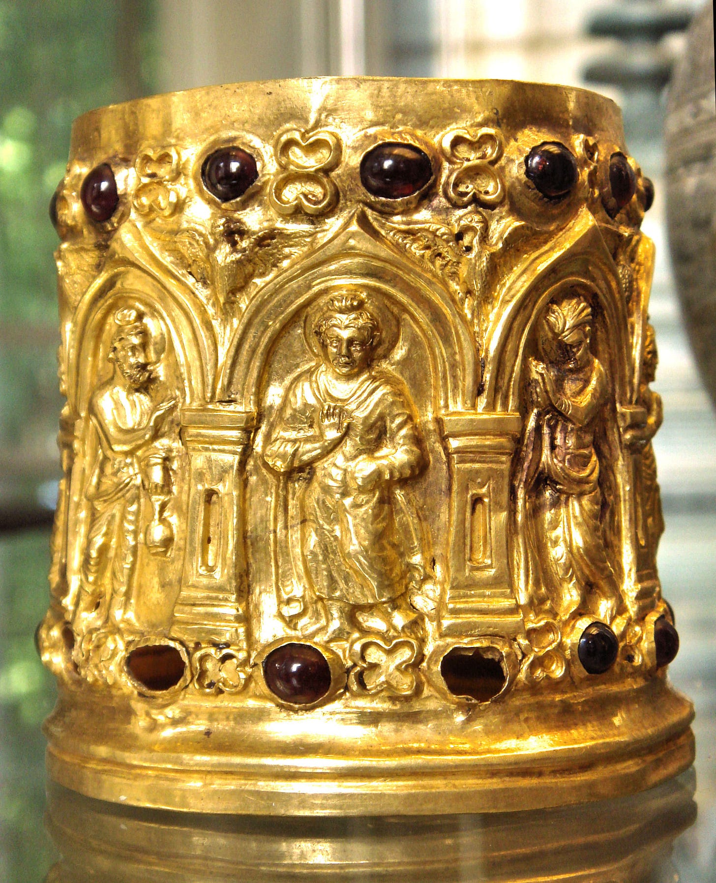 Photograph of golden cylindrical with a frieze of human figures and inlaid gems