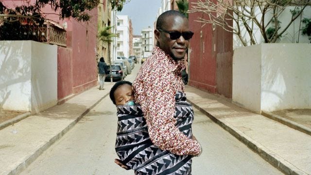 A Sengalese man carrying a sleepy baby on his back