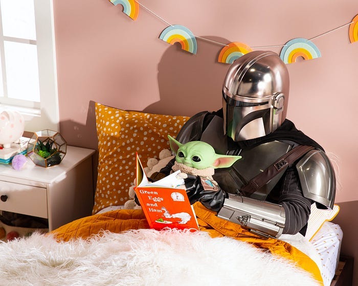 The Mandalorian reads ‘Green Eggs and Ham’ to Baby Yoda under a garland of rainbows. The Mandalorian reads ‘Green Eggs and Ham’ to Baby Yoda under a garland of rainbows.
