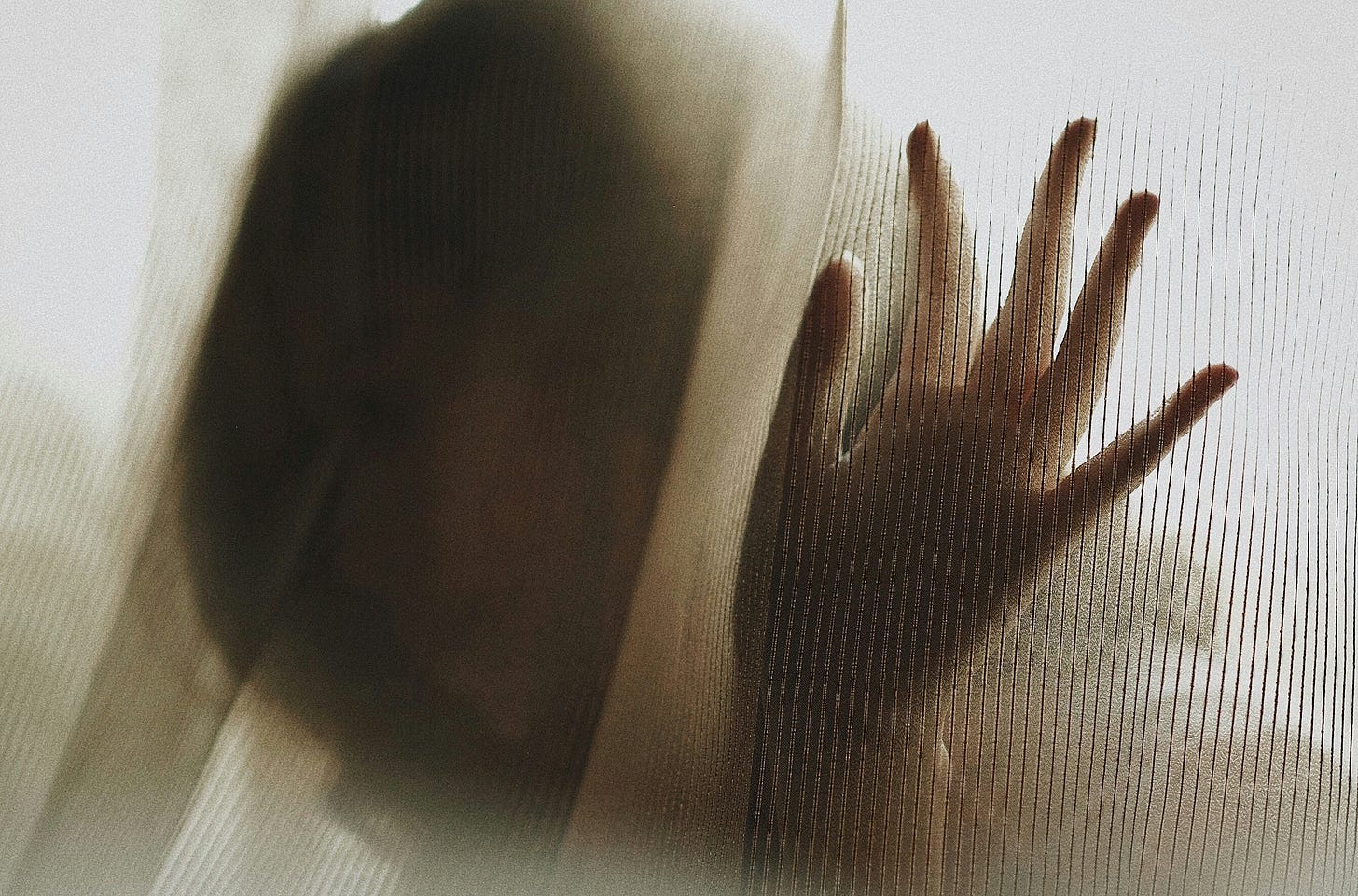 This image features an atmospheric and intimate composition of a hand pressing against a semi-transparent fabric. The soft light diffuses through the material, creating a moody and ethereal effect. The textures of the fabric and the silhouette of the figure evoke feelings of mystery and emotion.