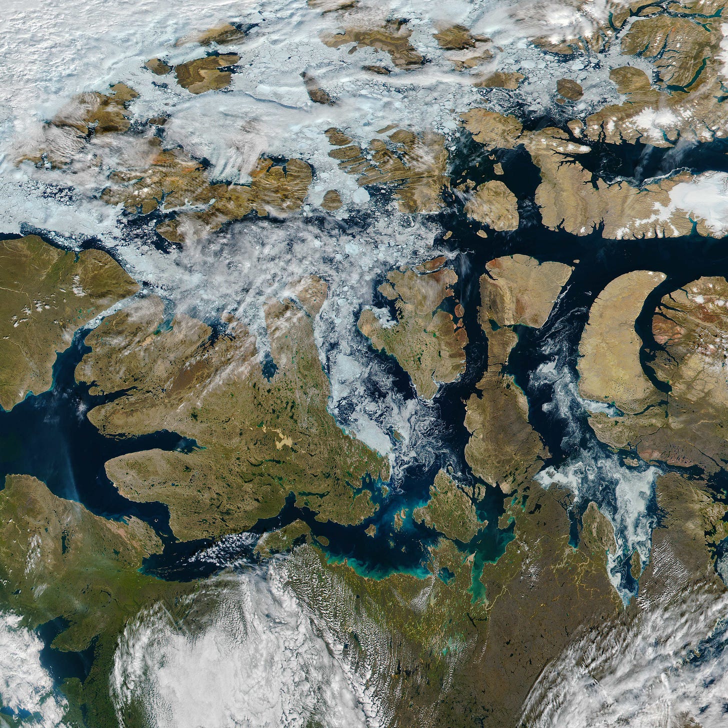 Satellite view of brown islands, dark blue sea, white ice, and some clouds