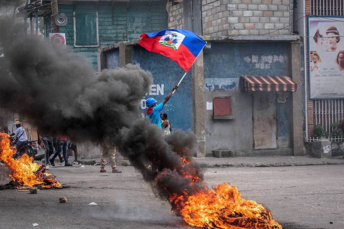 In this file photo from Aug. 14, 2023, a man with the Haitian flag in hand stands in the middle of a fire to ask for peace as violent gangs press attacks.