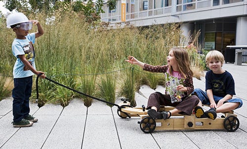 Three children on the walkway in New York City's High Line park. One pulls a makeshift wagon with one of the kit's cords; two others ride the wheeled structure they've built.