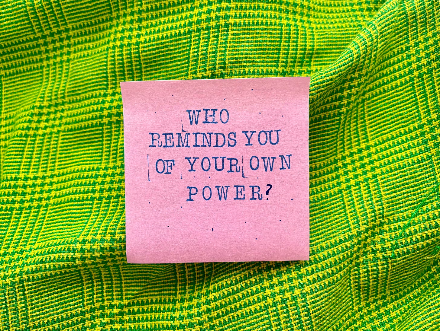 a pink post-it against green fabric that says in stamped letters "Who reminds you of your own power?"