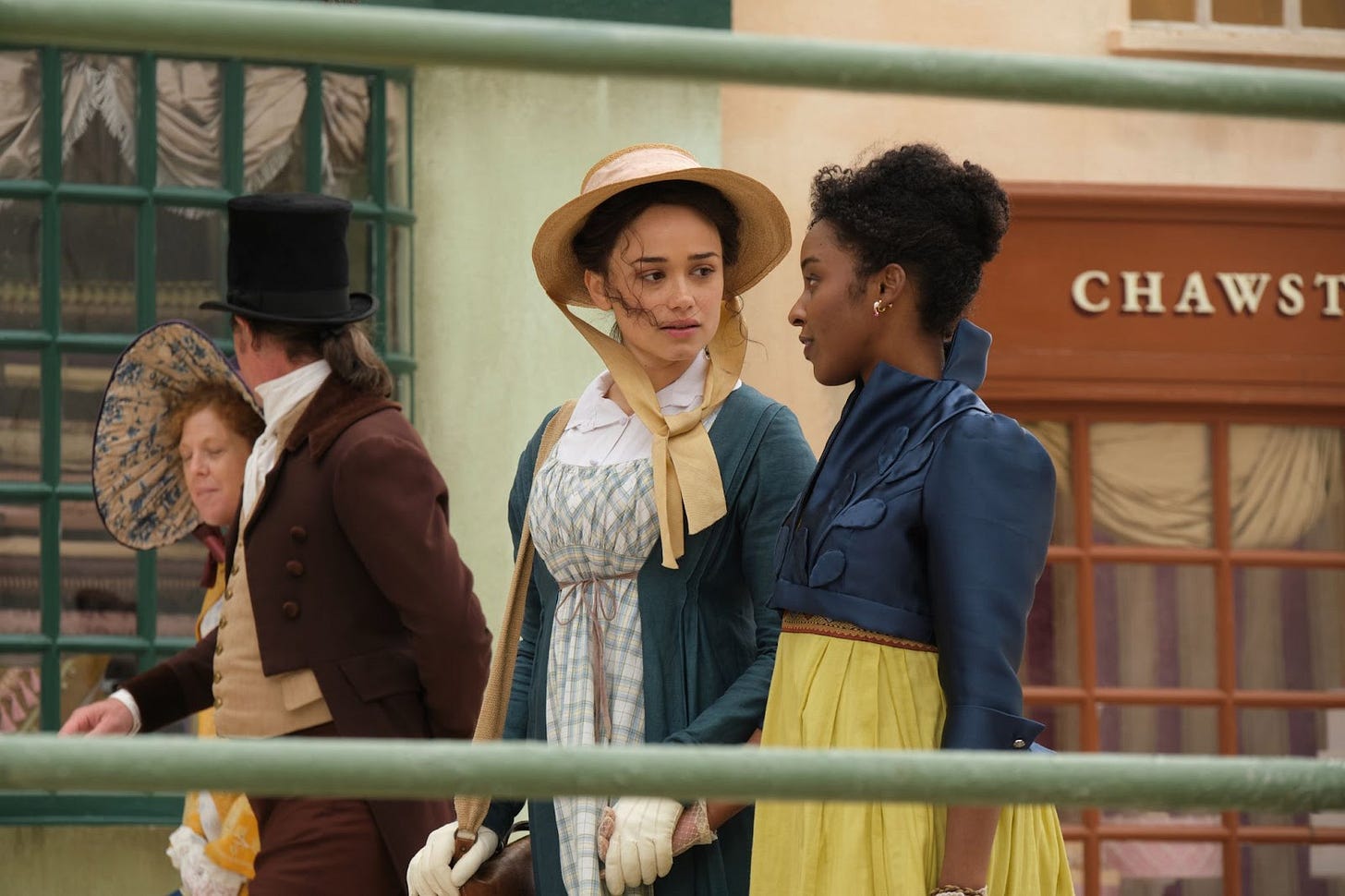 Pictures are two young women in Regency attire walking down a busy street scene in a Regency town. The photo features Rose Williams as Charlotte Heywood and she is holding hands with Crystal Clarke's Georgiana Lambe, in this photo from the PBS Masterpiece series. Pictures are two young women in Regency attire walking down a busy street scene in a Regency town. The photo features Rose Williams as Charlotte Heywood and she is holding hands with Crystal Clarke's Georgiana Lambe, in this photo from the PBS Masterpiece series.