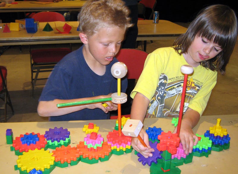 Two young boys intensely focused on creating a model using tinker toys and plastic gears that fit together.