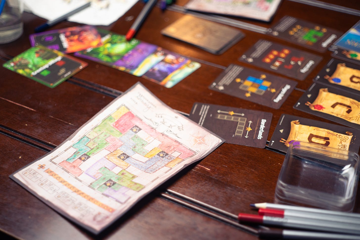 The map-drawing game Cartographers on a table. You can see a hand-drawn map, cards, and colored pencils.