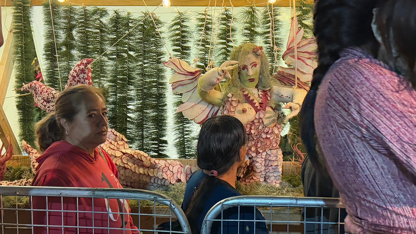 People lined up behind a metal barrier in front of a radish display shaped like a mermaid.