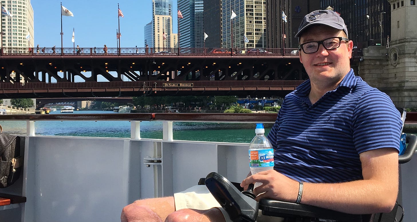 John sitting on a boat in his wheelchair on the Chicago river, with the city skyline in the background.
