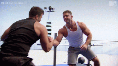two muscular white guys in workout gear share a brotherly hug on the beach