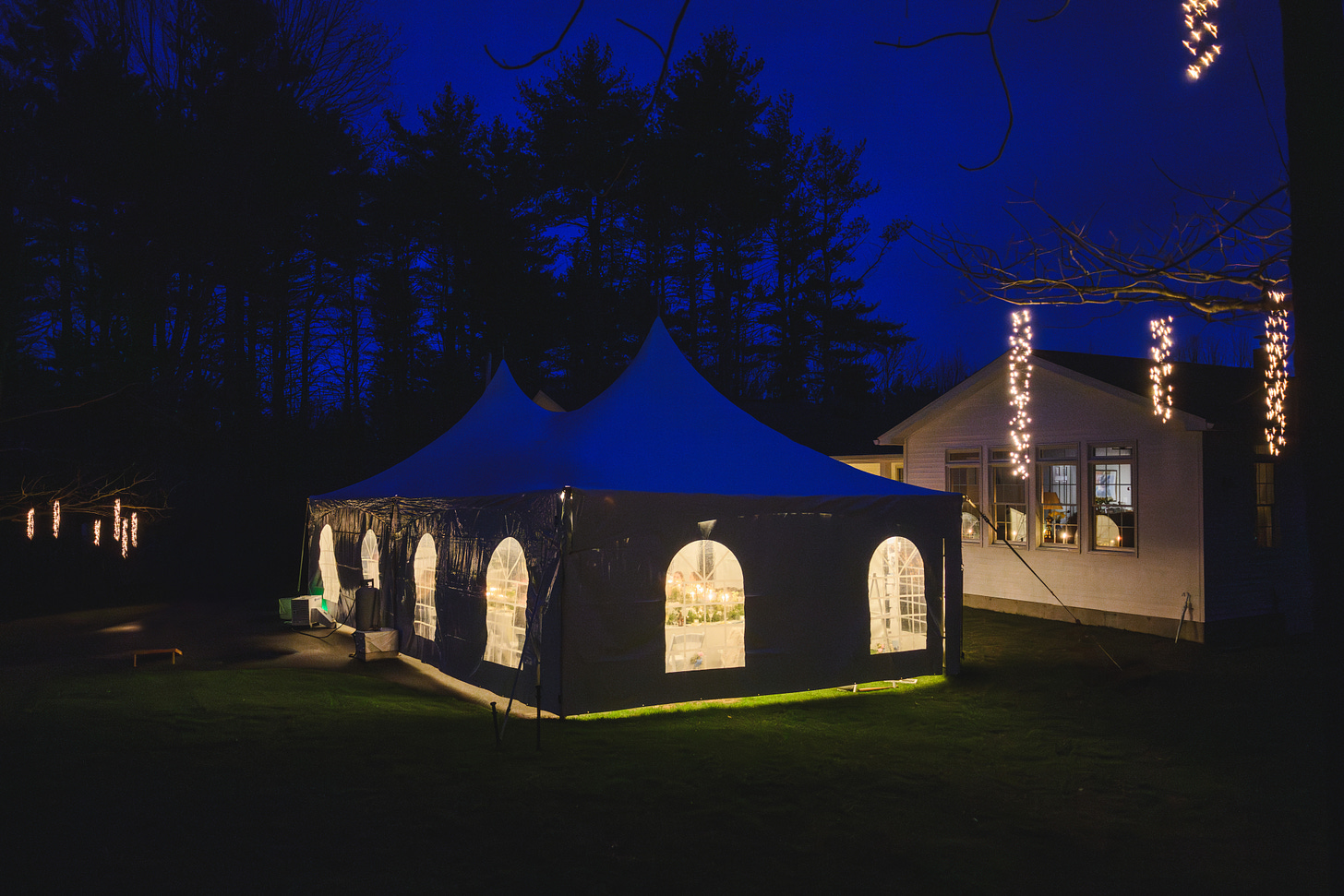 A nighttime photo of a wedding reception tent with hanging lights in the trees around it