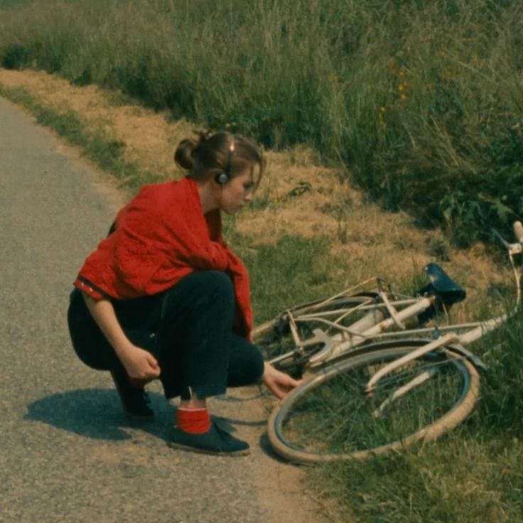 This may contain: a woman kneeling down next to a bike on the side of a road with it's front wheel missing