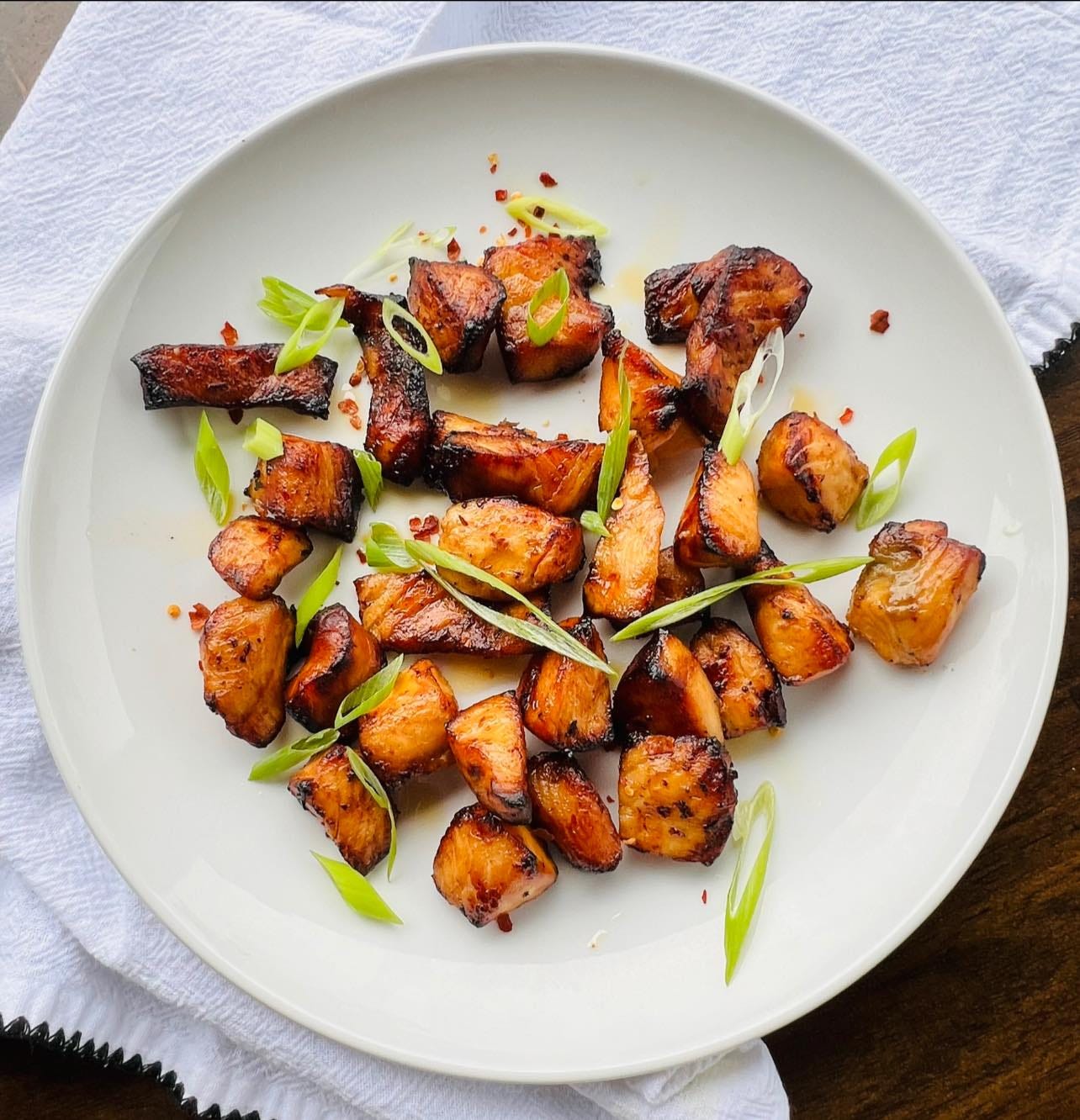 Ingredients:  1 pound salmon fillets, cut into bite-sized cubes  2 tablespoons rice vinegar  1 tablespoon soy sauce (low-sodium optional)  1 tablespoon sriracha  1 to 2 tablespoons honey  1 clove garlic, minced  1 teaspoon ginger, grated  1 teaspoon sesame oil (optional)  Sesame seeds and green onions (for garnish)