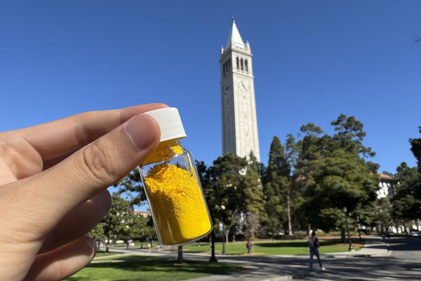 A hand holds a vial of yellow powder.