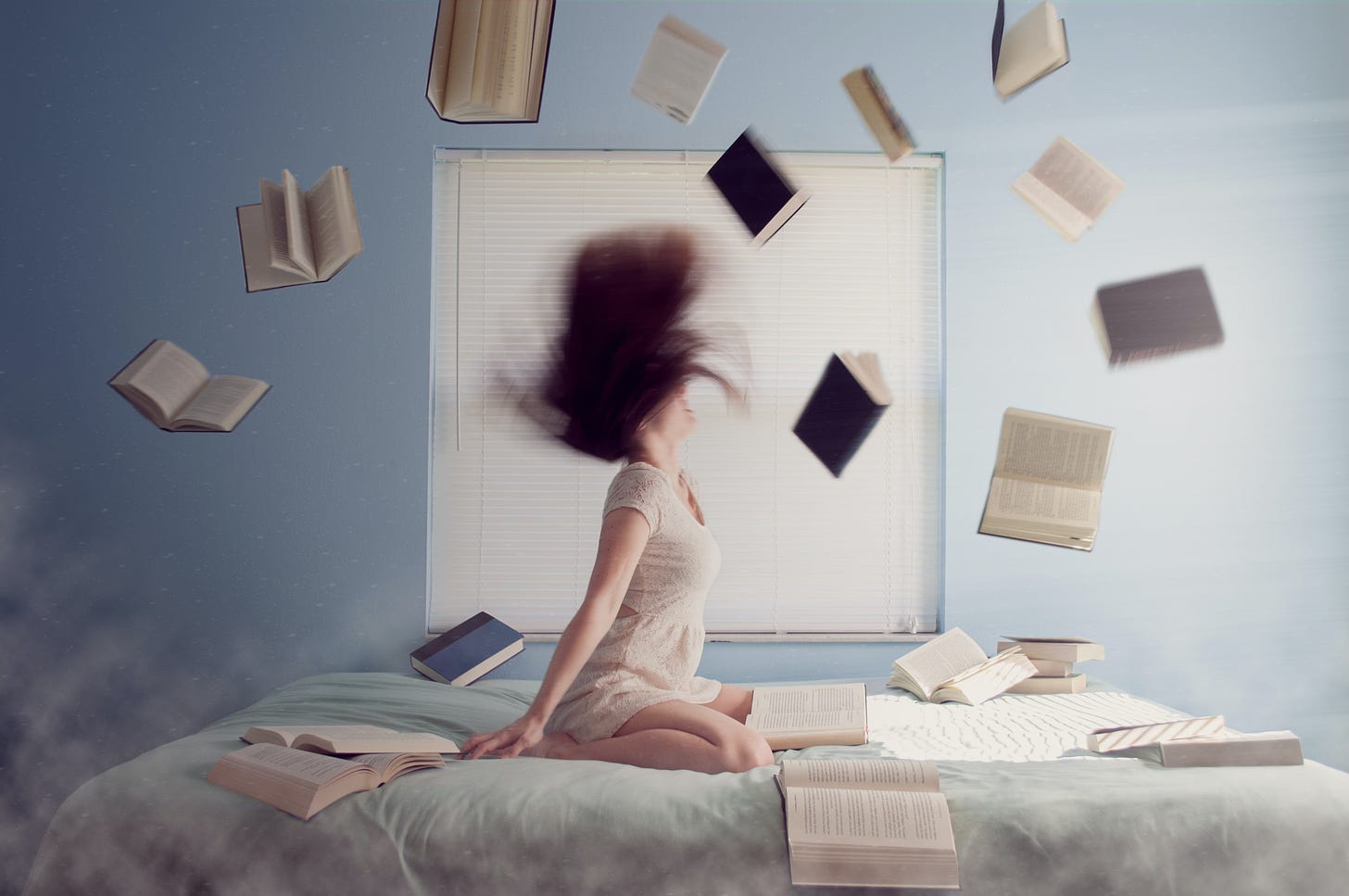 A white woman in a white dress, kneeling on a bed, throwing her hair back. Around her, books are floating. Behind her, a blue wall and a white-shaded window.