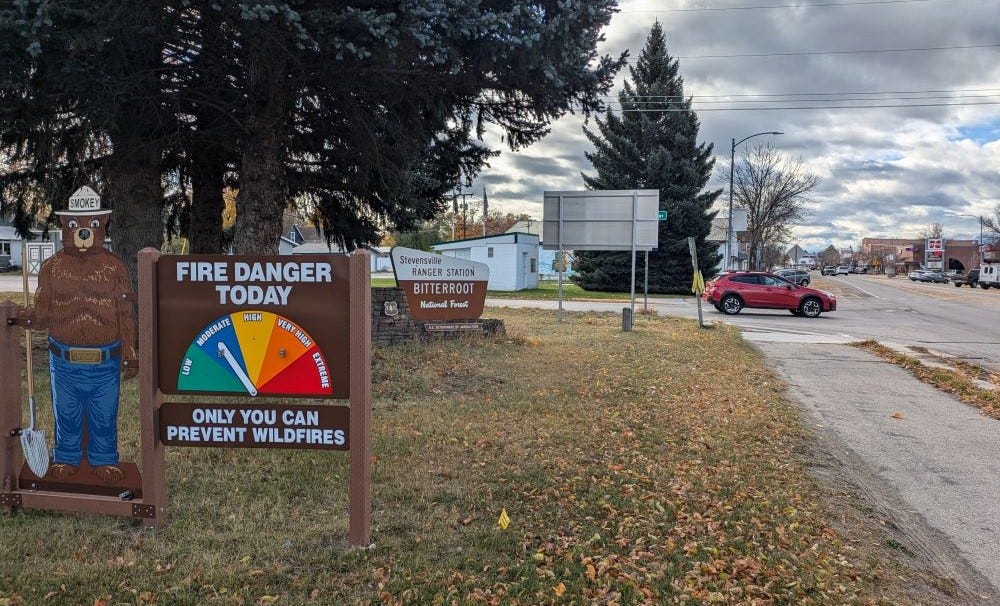 The fire danger sign (set to moderate) in front of the Stevensville Ranger Station, with a quaint downtown of brick buildings in the background