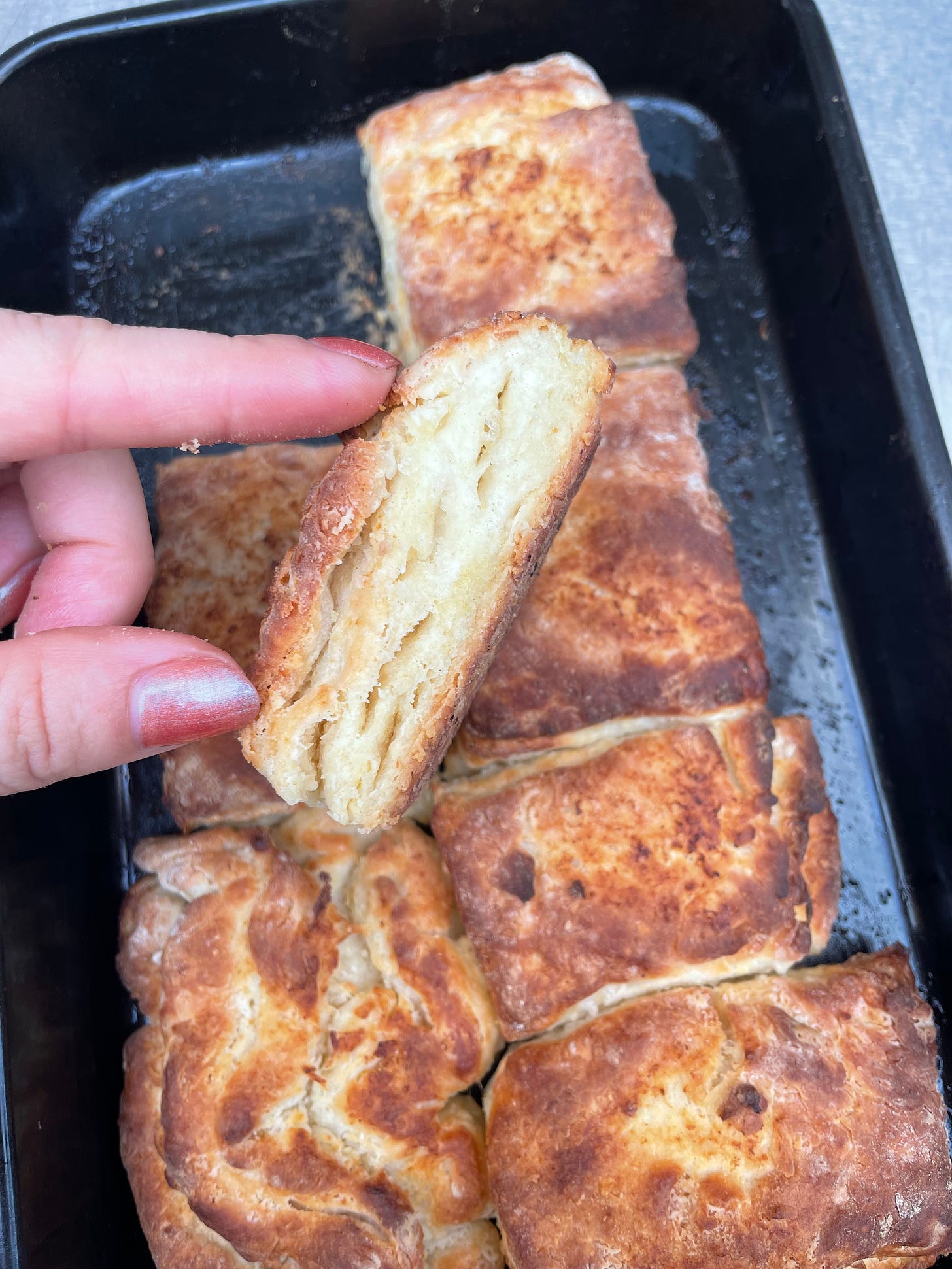 a hand holding a cooked biscuit so that the cross-section is visible. in the background is a pan containing other scones closely nestled together