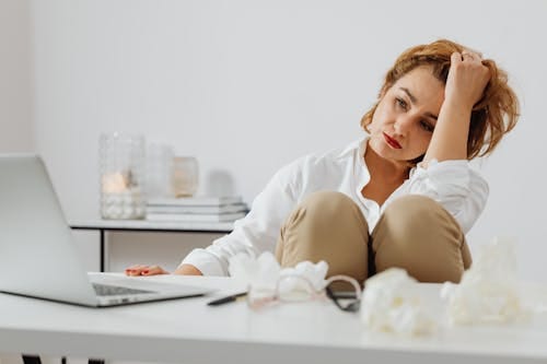 Free A woman looks stressed while working remotely from home, surrounded by tissues. Stock Photo