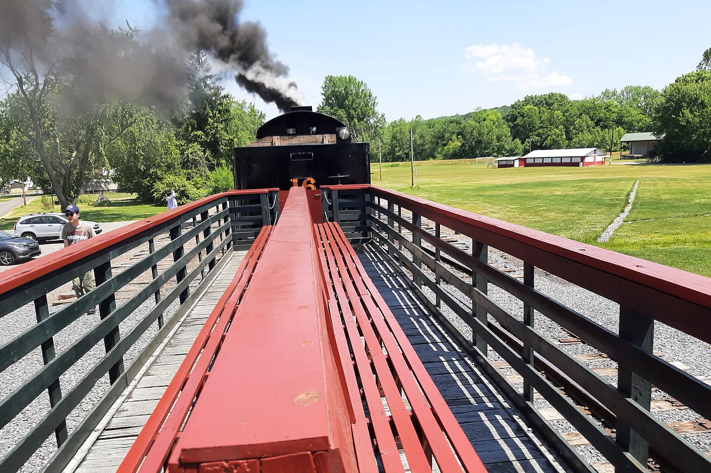 Red benches in an open car behind a steam engine.