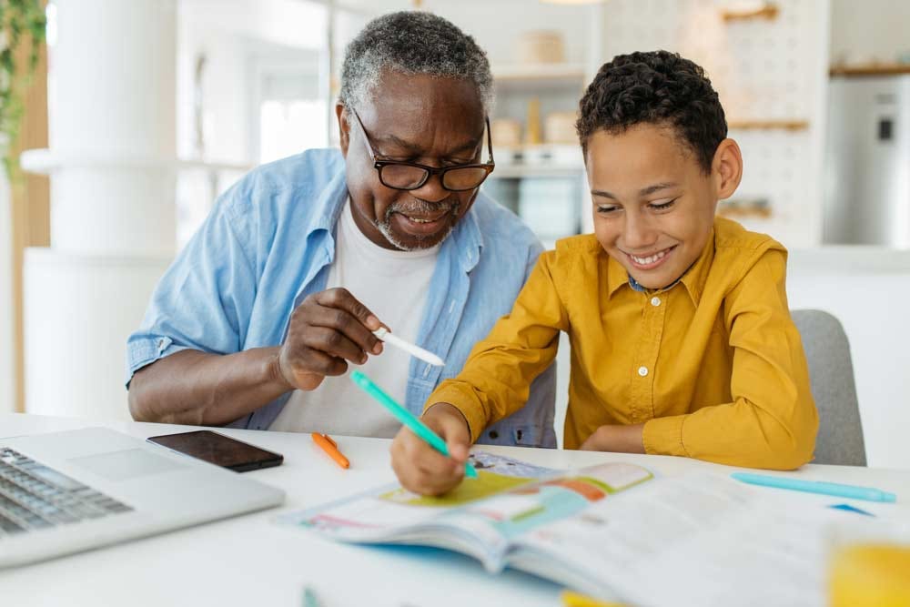 Elder teaching grandson from a school workbook.