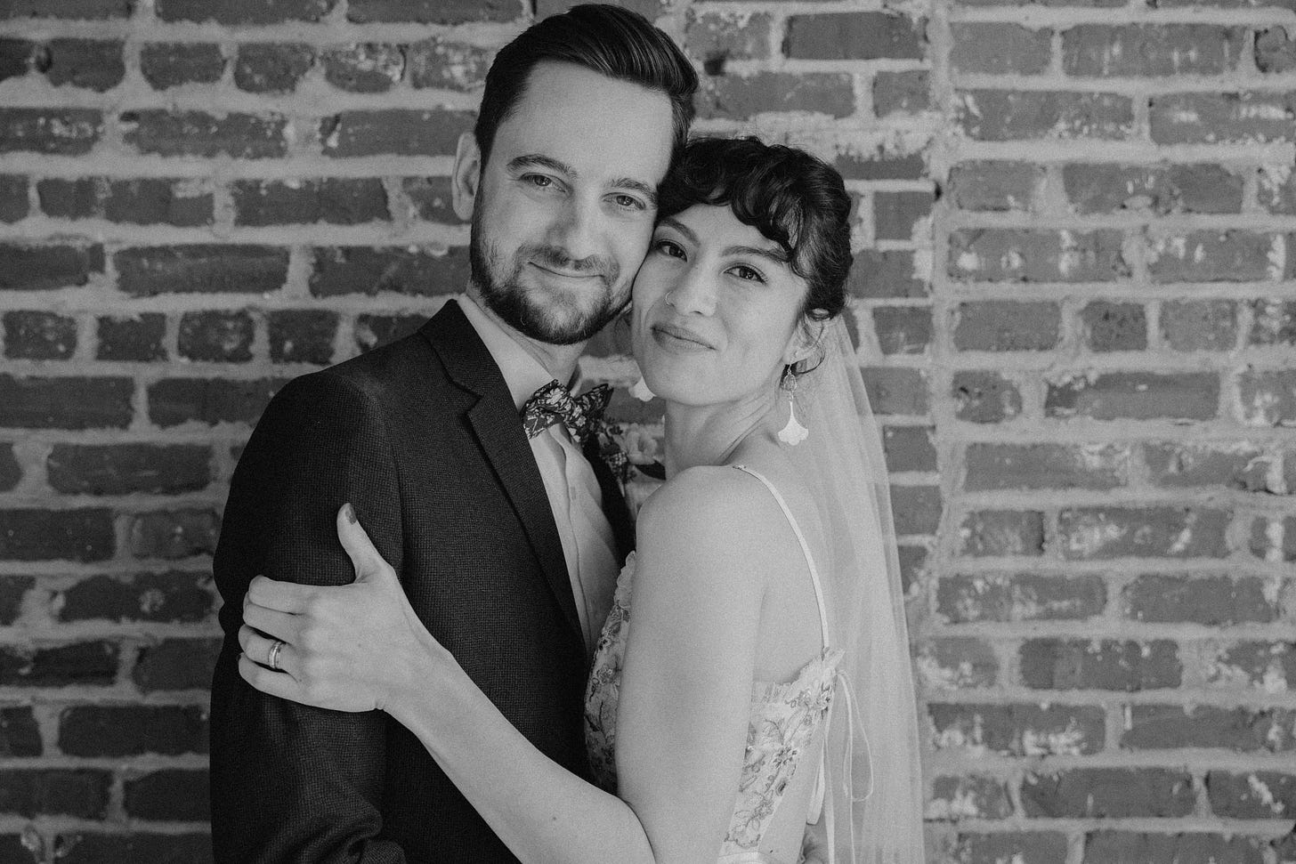 A wedding portrait of the author, Erika, with her husband, Aaron. Erika is embracing Aaron as they both look into the camera with soft smiles.