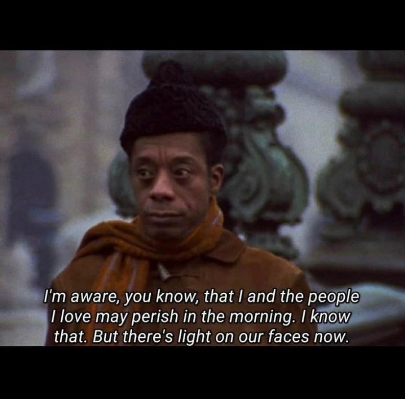 Color photo of James Baldwin wearing a black hat, brown jacket and scarf behind text added on top of the photo reading, “I’m aware, you know, that I and the people I love may perish in the morning. I know that. But there’s light on our faces now.”