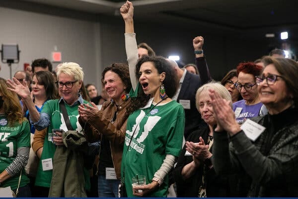 A crowd, mostly female and some in green T-shirts with reproductive rights slogans, clapping, cheering and raising fists.