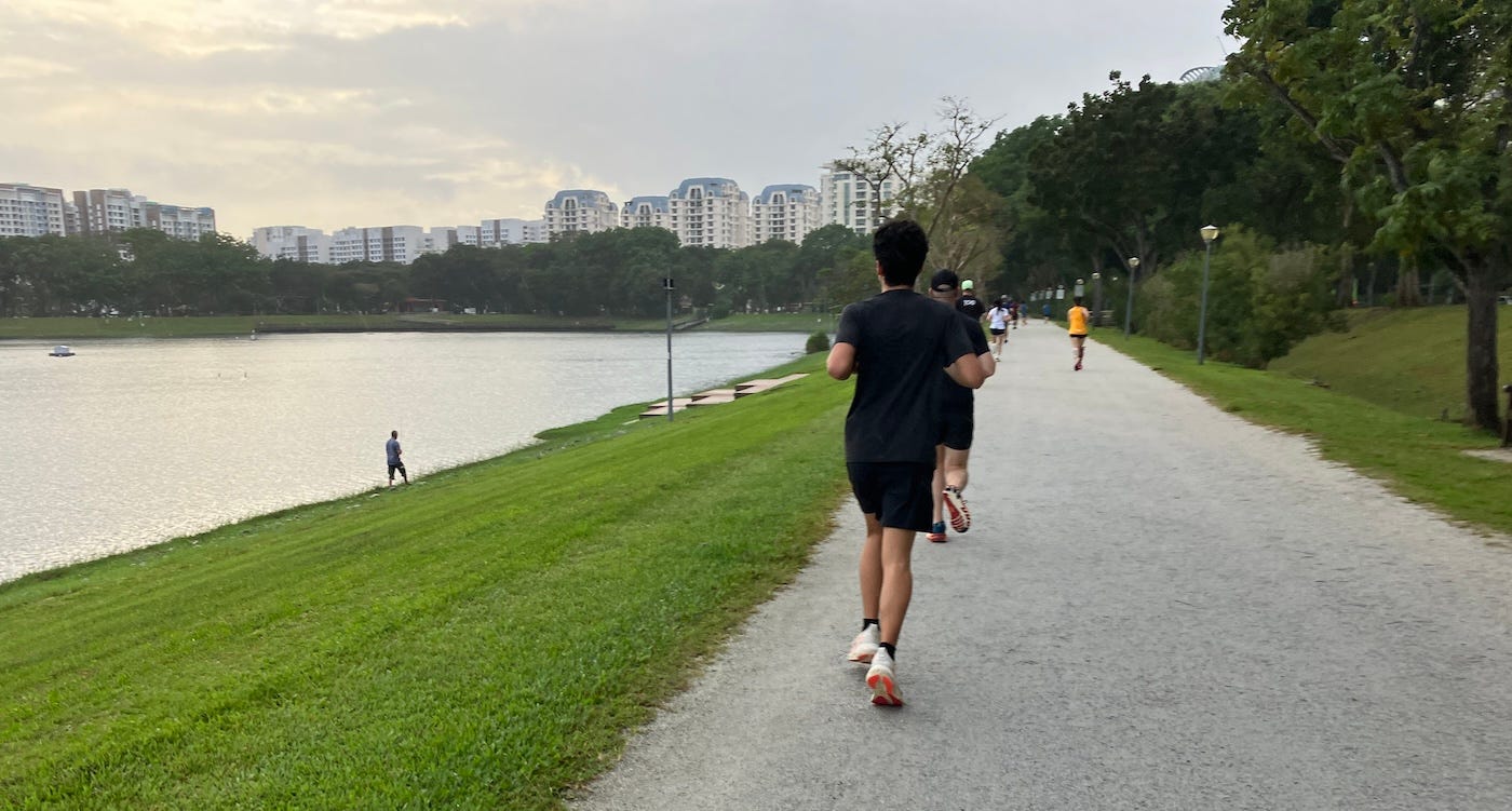 Runners on a high, wide path, bordered by coarse grass, with a large reservoir to the left.