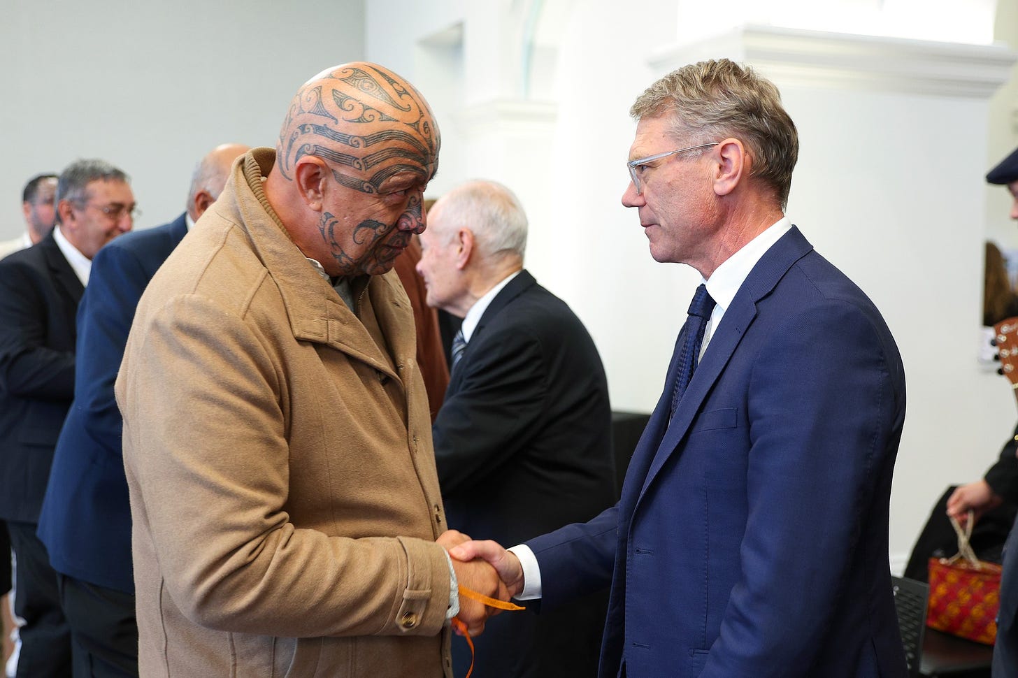 Paul Golsmith shaking hands with Māori man who is looking at him suspiciously.