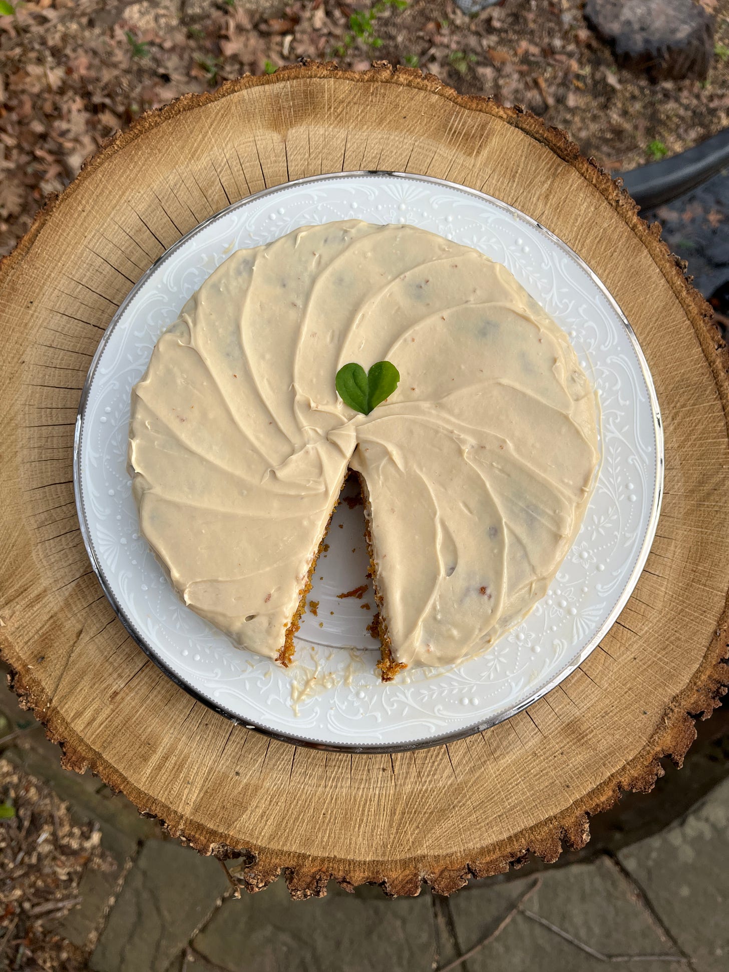 single layer carrot cake with cream cheese frosting, decorated with a heart shaped sorrel leaf, one slice removed, seen from above 
