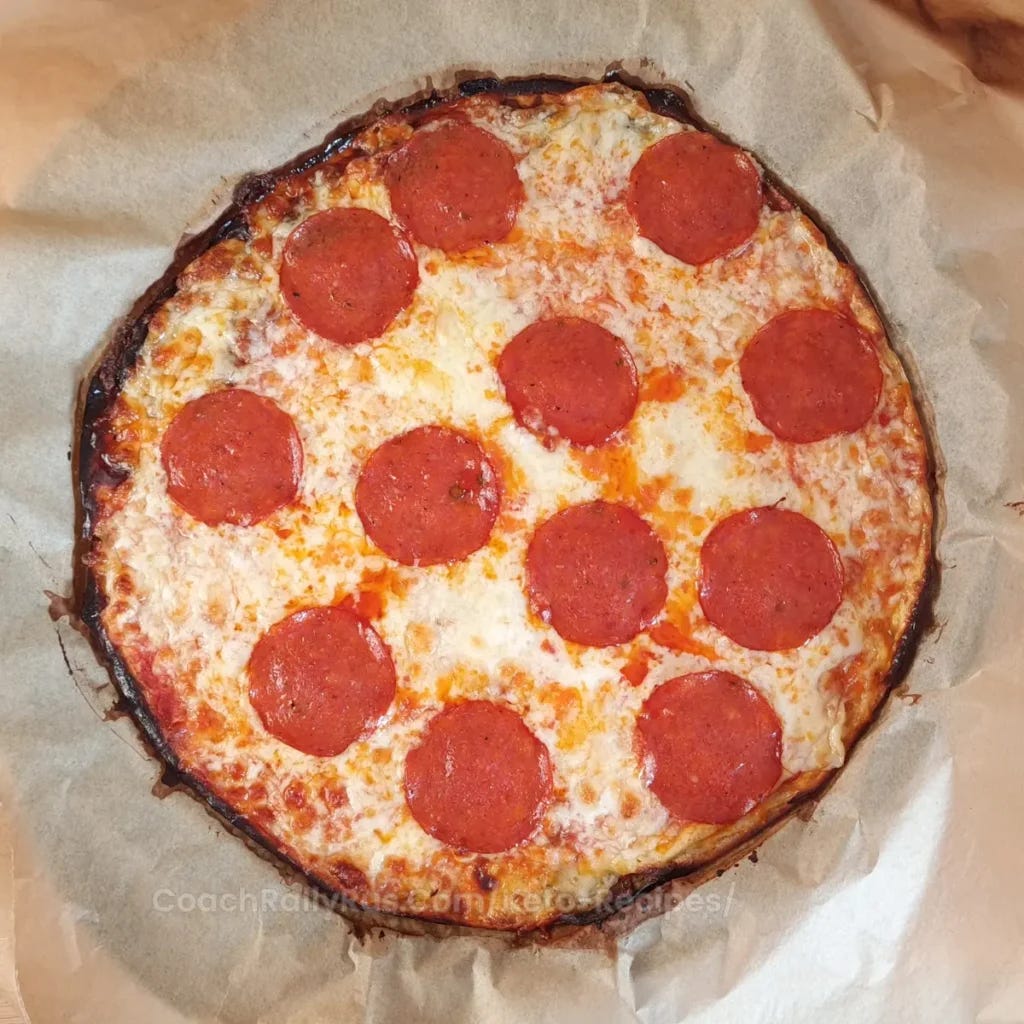 A freshly baked pizza with a golden-brown crust and melted cheese, topped with large pepperoni slices. The pizza is cut into triangular slices and rests on parchment paper with a pizza cutter on top, suggesting it is a homemade or artisanal cottage cheese pizza.