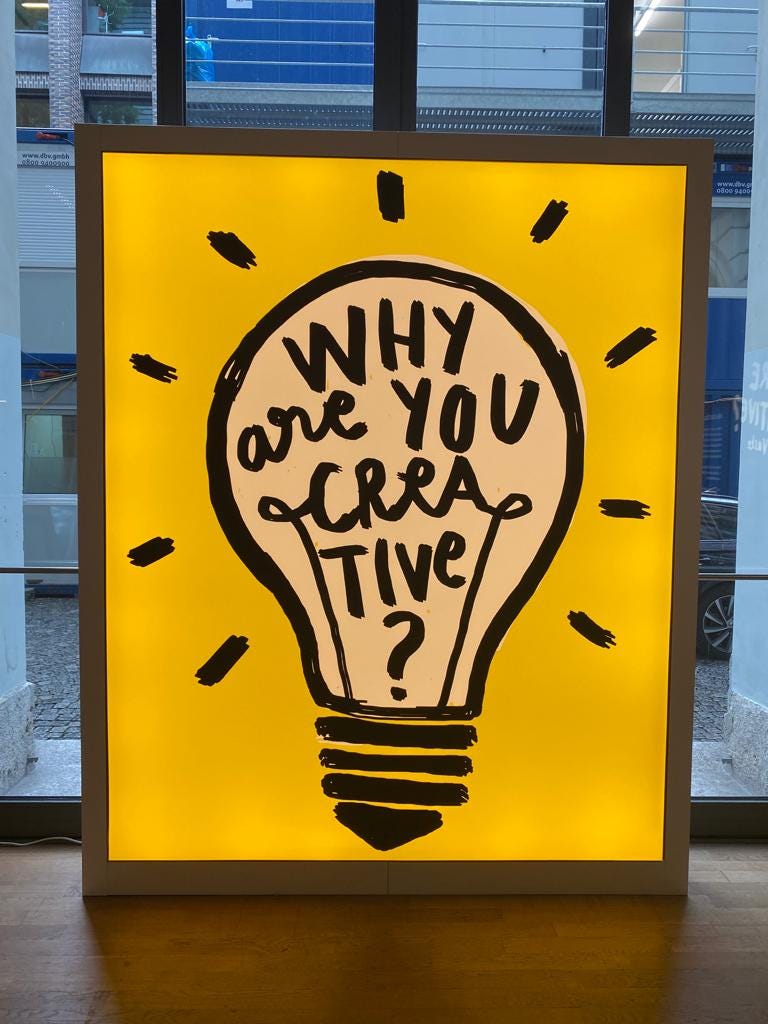 Cartaz da exposição "Why are you creative?", uma lâmpada desenhada em fundo amarelo.