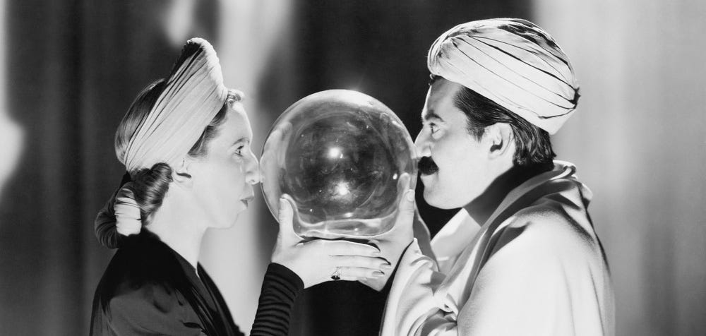 Foto em preto e branco e um homem e uma mulher próximos, um de frente para o outro, eles seguram juntos uma bola de cristal que se interpõe entre seus rostos, ambos olham para a bola de cristal.