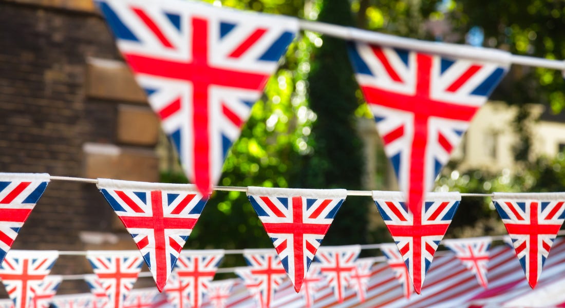 An outdoor area with Union Jack bunting hanging in front of a brown brick building and a green tree