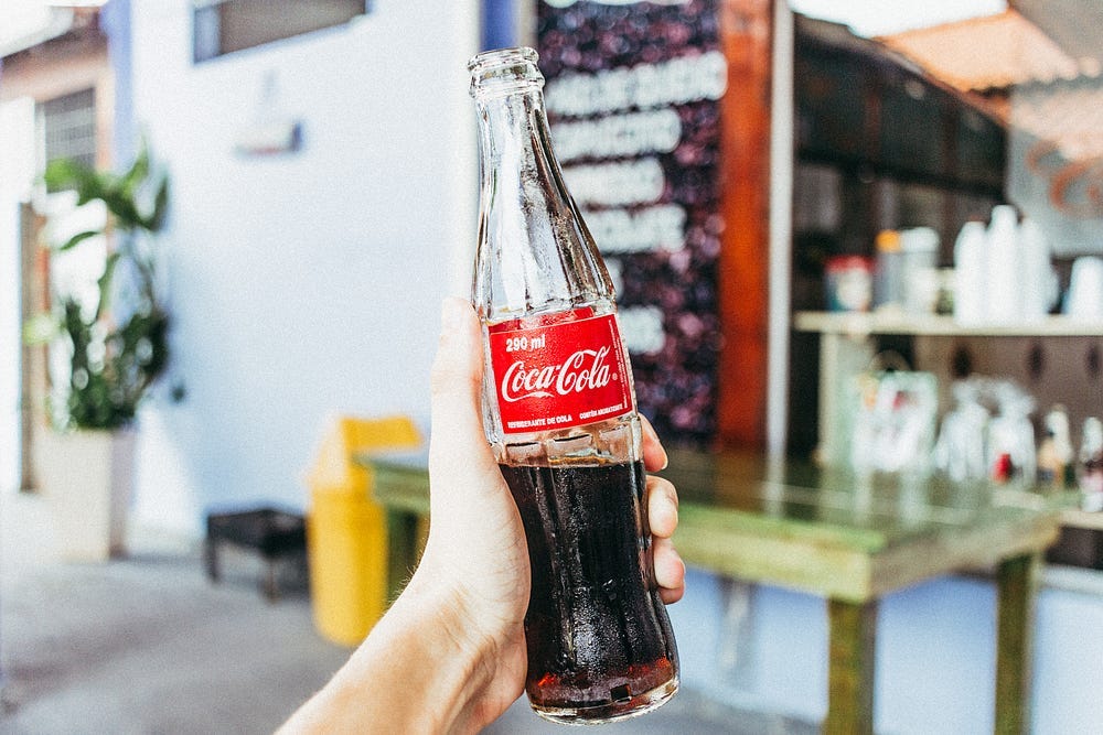 A hand holding the Classic Coca-cola glass bottle, raising the bottle to the air