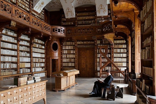 A man sits in an ornate library, reading a book