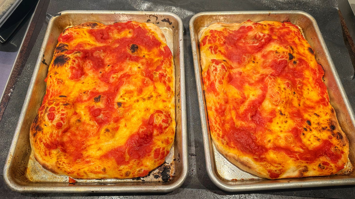 Two parbaked doughs, side by side on sheet pans. There are puffed-up bits of the dough that are slightly charred.