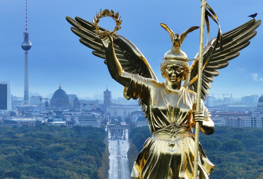 A close view of a large golden statue of an angel, with the Berlin skyline in the background.