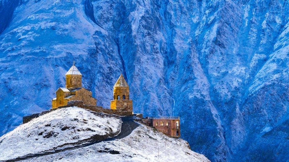 14th Century Tsminda Sameba Church, (Holy Trinity Church), Gergeti, at 2200m above Kazbegi, in dawn light against Mount Kazbek, Georgia