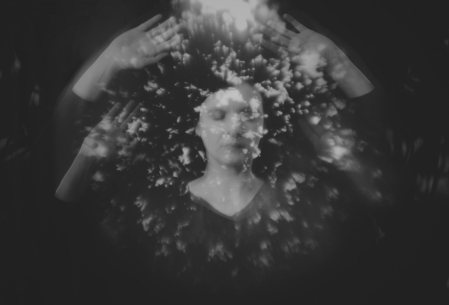 Image of a person with closed eyes holding her arms up high in the dark while lights is flooding in from above