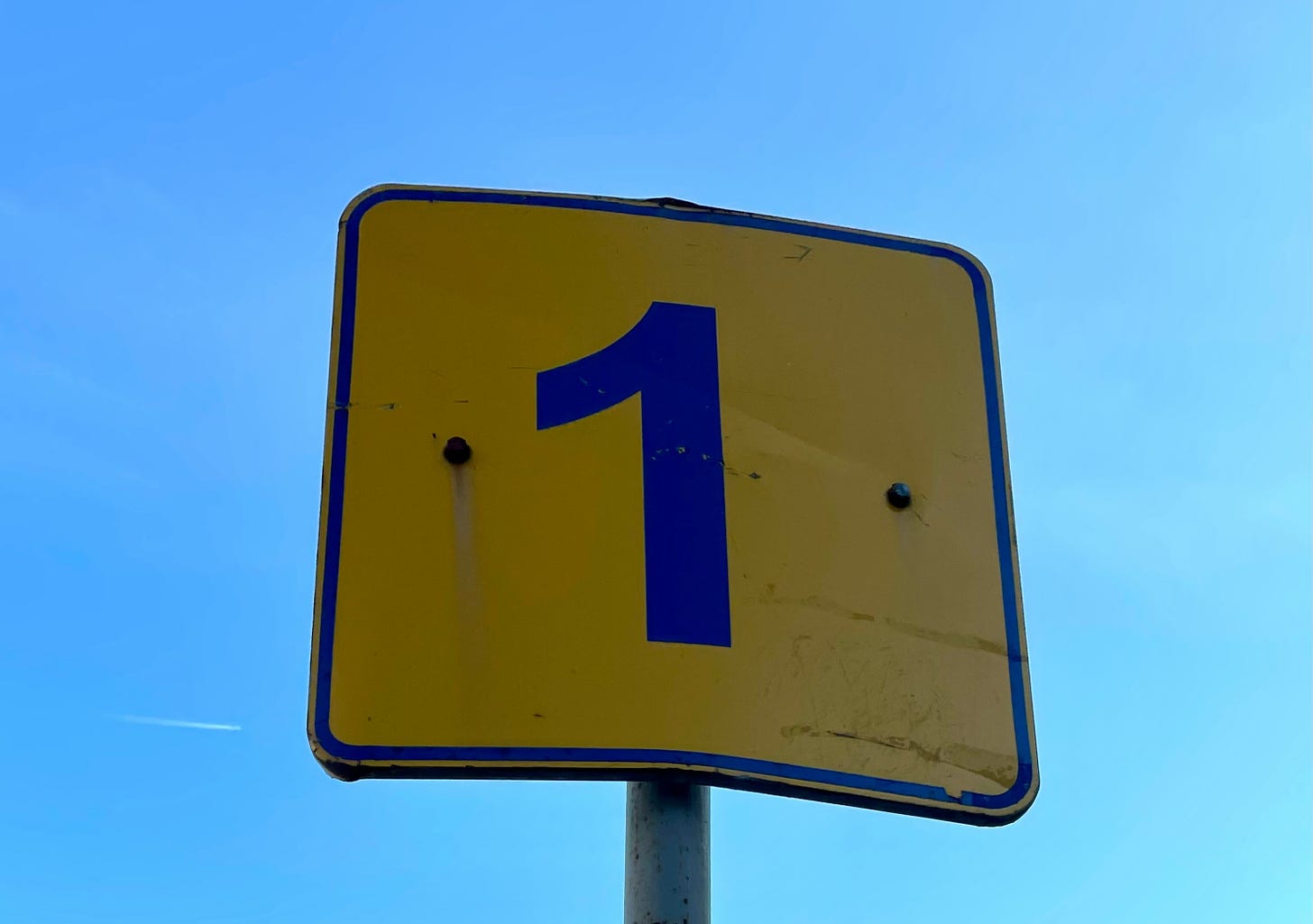 A yellow road sign with the number one in blue in the centre.