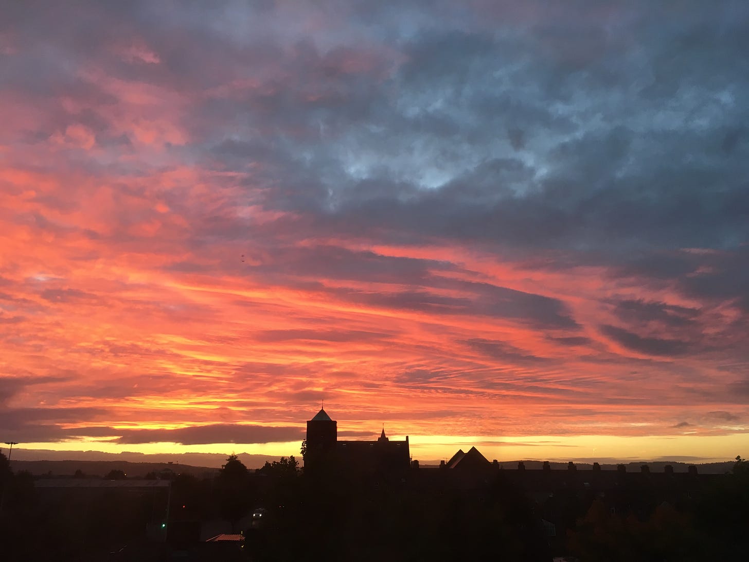 Photograph of a brilliant orange sunrise filling the sky over a steeple