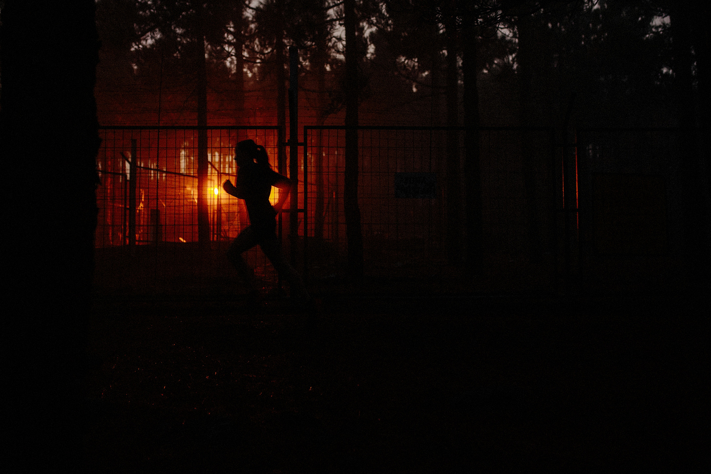 A female runner in front of a fence covered in evening sun