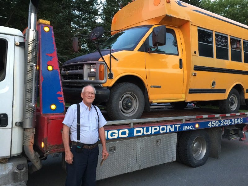 Short schoolbus on flatbed after breakdown, towtruck driver standing in front.