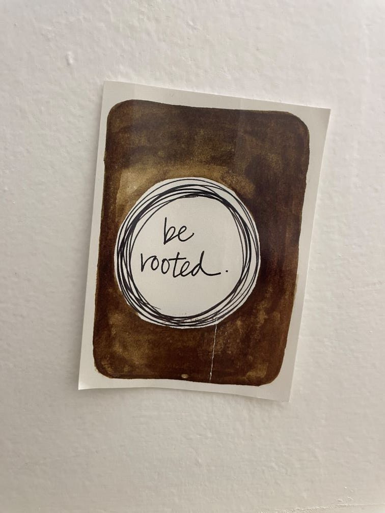 small card on white wall. card is brown with circle in center containing the words "be rooted"