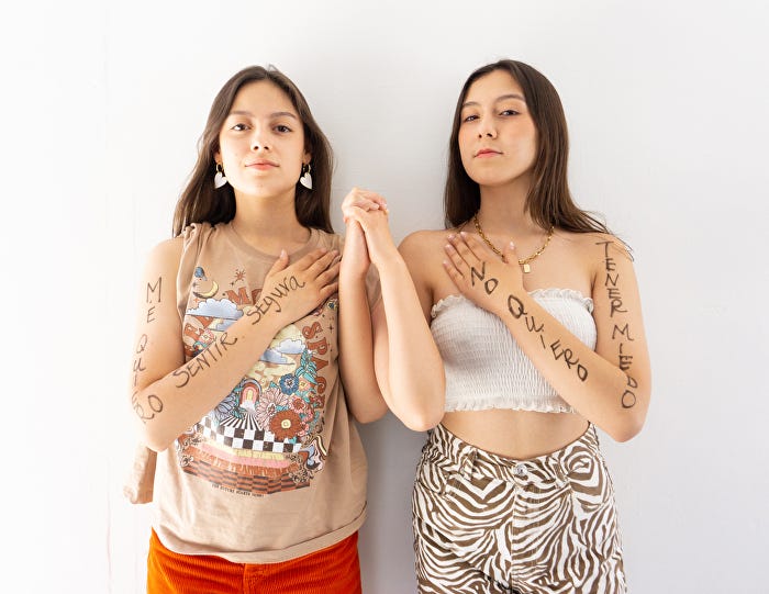 Two teenage sisters holding hands with bold black ink written on their arms