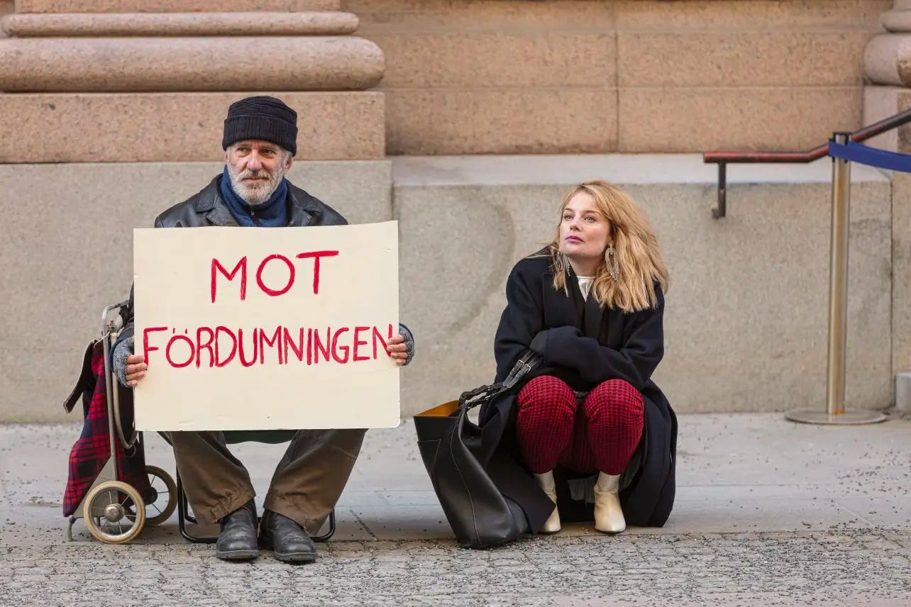 Homem carregando placa em sueco onde se lê, em tradução livre, "contra a estupidez".