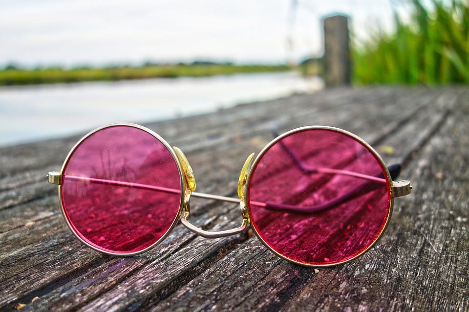 A pair of rose-tinted sunglasses sitting on a wooden jetty