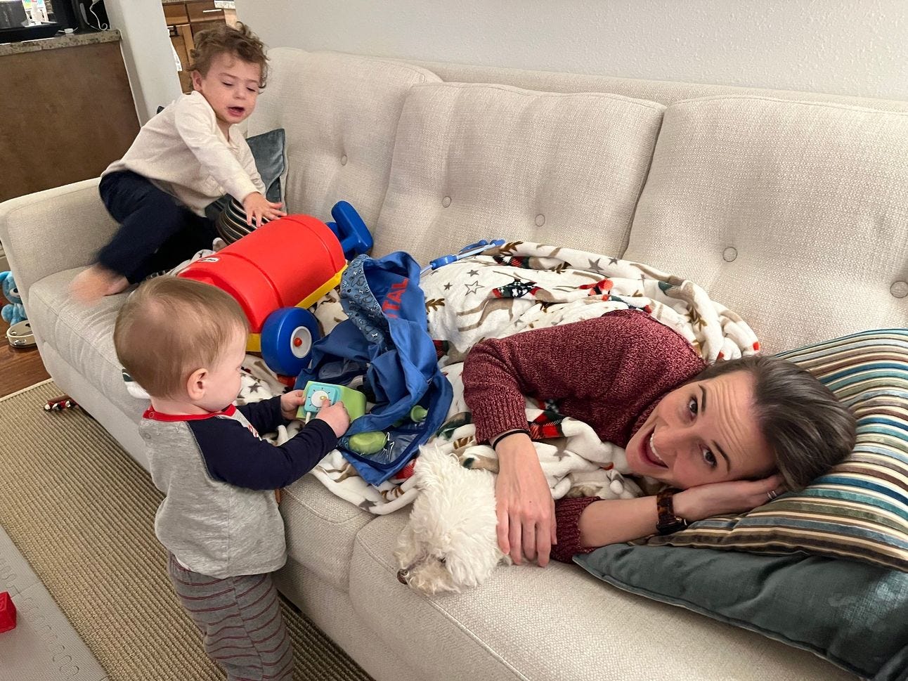 A woman laying on a couch with her two kids beside her. A woman laying on a couch with her two kids beside her.
